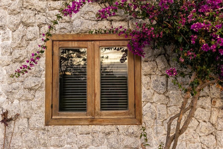 Fenêtre en bois à deux battants dans un mur de pierre claire garni de fleurs violettes