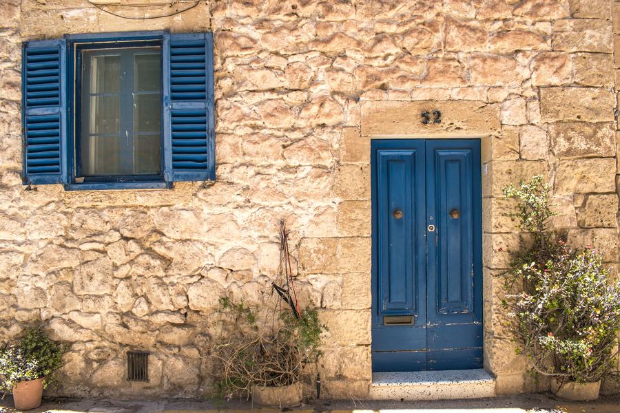 Façade en pierre claire avec une porte d'entrée bleue et une fenêtre aux volets battants bleus