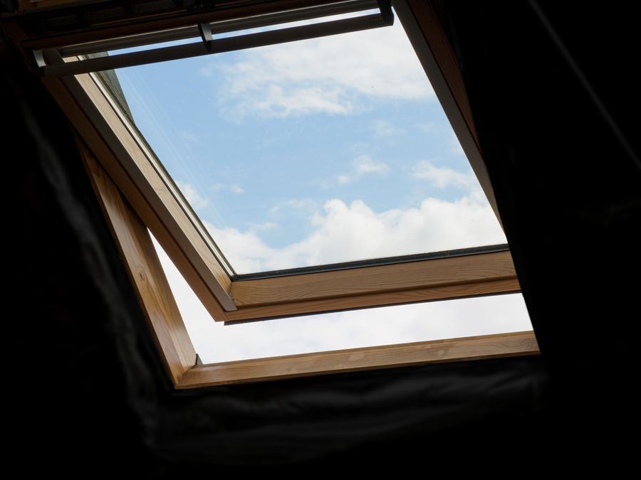 Fenêtre de toit ouverte vue d'en dessous, avec le ciel bleu et quelques nuages à travers