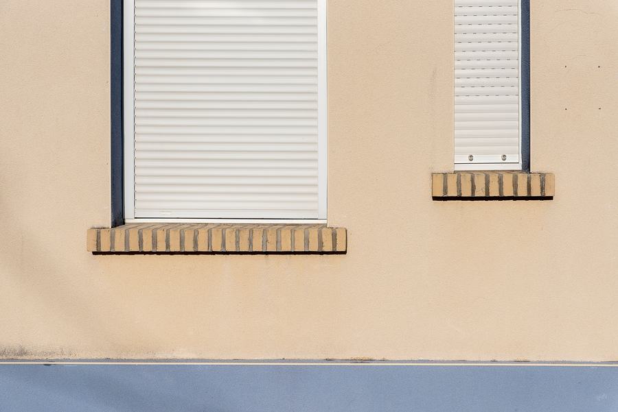 Façade beige à deux fenêtres, dont l'une est fermée par un volet roulant blanc